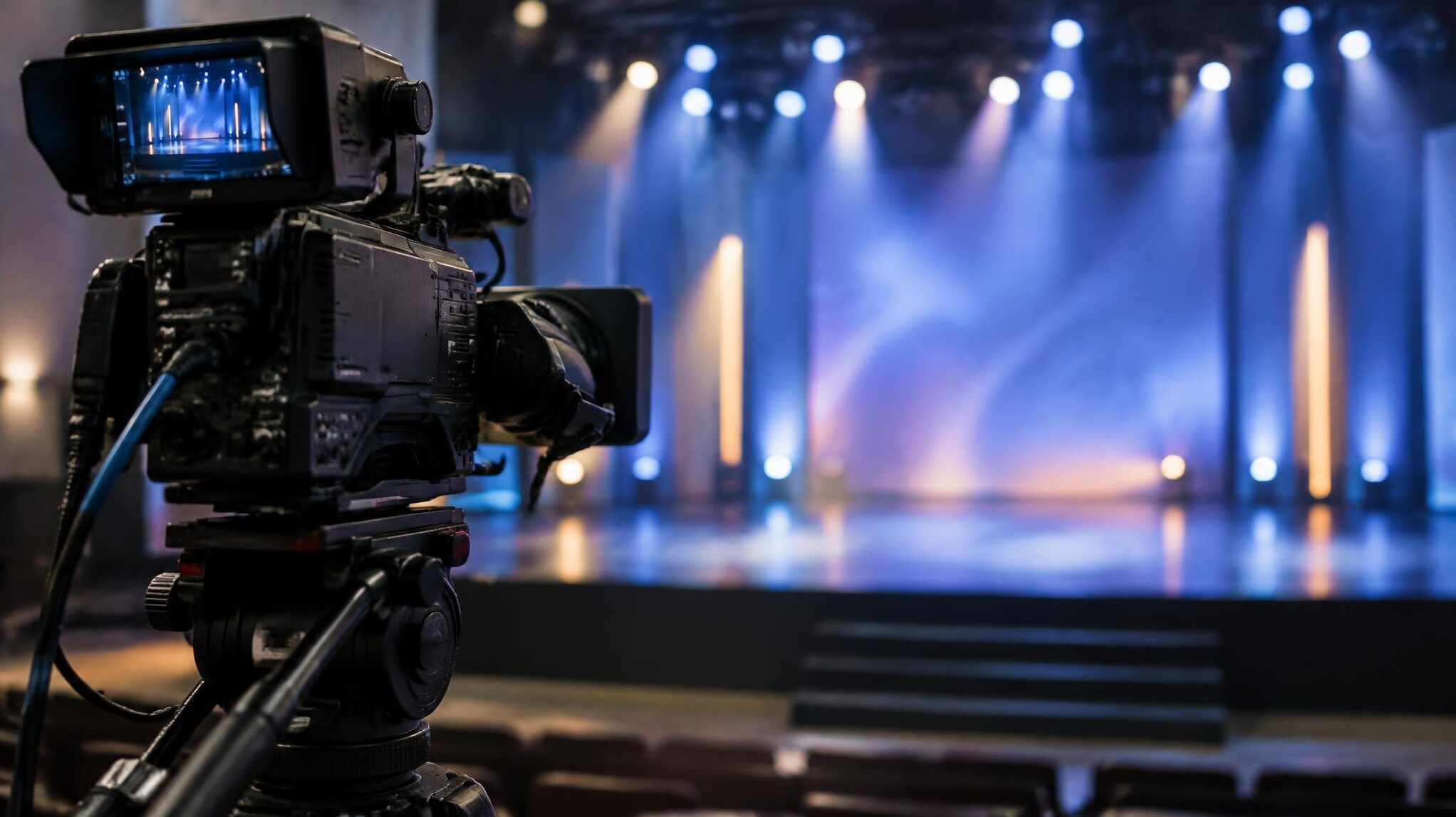 Broadcast camera on a tripod facing an empty stage